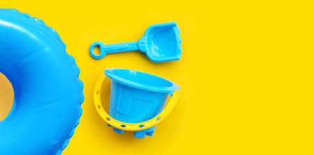 Plastic toys, Swimming pool ring with bucket and shovel for sand on yellow surface.の写真素材