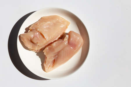 Uncooked raw chicken breast fillets in white plate on white background.の写真素材
