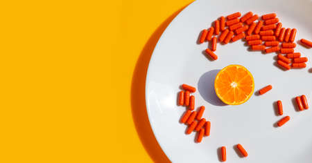 Orange fruit with capsule pills in white plate on orange background.の写真素材
