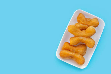 Deep-fried dough sticks or chinese bread sticks in white plate on blue background.