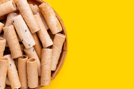 Thai crispy coconut rolls in bamboo basket on yellow background.