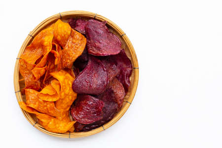 Purple and yellow sweet potato chips in bamboo basket on white background.の写真素材