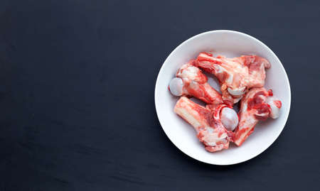 Raw pork bones in white bowl on dark background.の写真素材