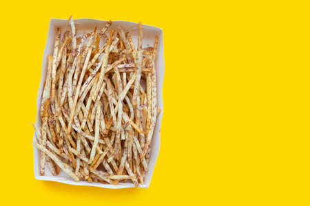 Fried taro sticks in paper box on yellow background.