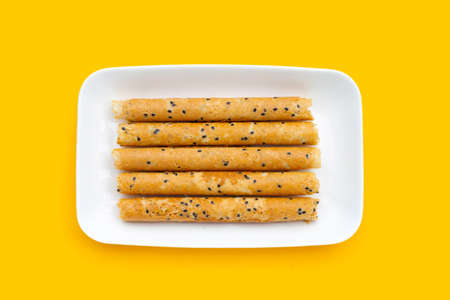 Crispy egg rolls in white plate on yellow background.