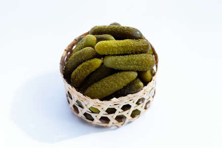 Pickled gherkins or cucumbers in bamboo basket on white background.