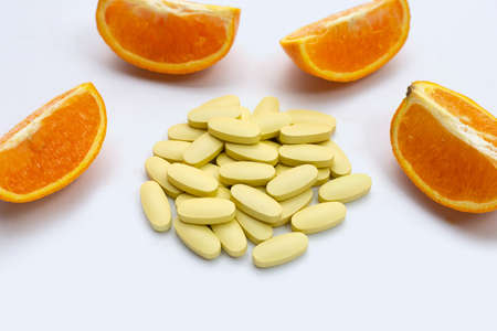 Vitamin c pills with orange fruit on white background.