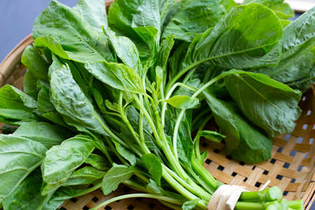 Green spinach in bamboo basket on dark background.