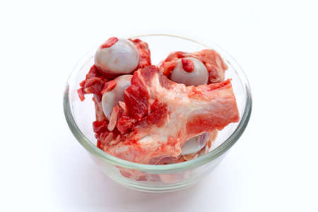 Raw pork bone in glass bowl on white background.