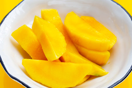 Yellow mango slices in bowl on yellow background.の写真素材