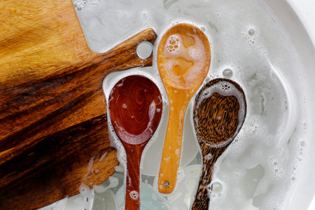 Wooden spoon, cutting board and dishes in water and bubbles of dishwashing liquidの写真素材