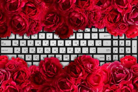 Modern black and laptop keyboard with bush of red rose flowers backgroundの写真素材