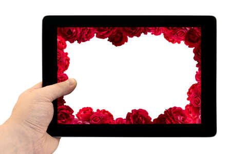 Tablet PC in hand with frame with bush of red rose flowers background on screen isolated on white