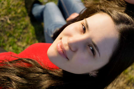 Portrait of young brunette girl in jeans and red jacket on grassの写真素材