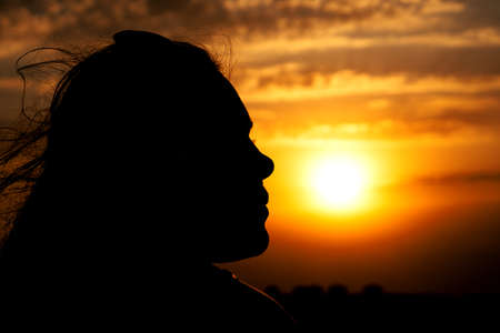 Young girl face silhouette looking on beautiful cloudy sky with orange sunsetの写真素材