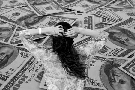 Money problem: Young brunette girl in bikini and pareo on background of mount of hundred dollar banknotes black and whiteの写真素材