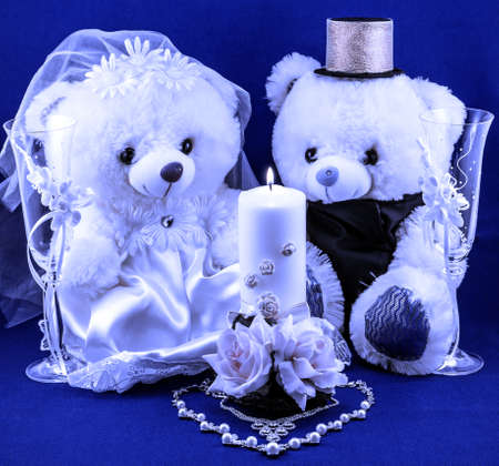 Wedding setting: hand made boy and girl teddies, white and gold candle, wedding glasses and pearl silver necklace in form of heart on textured blue background cold filteredの写真素材