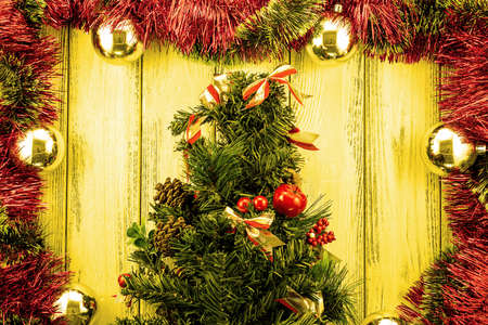 New year theme christmas tree with red and green decoration and golden balls on yellow retro stylized wood backgroundの写真素材
