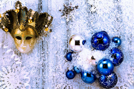 New year theme: Christmas tree white and silver decorations, blue balls, snow, snowflakes, serpentine and golden mask on white retro stylized wood background with blue backlightの写真素材