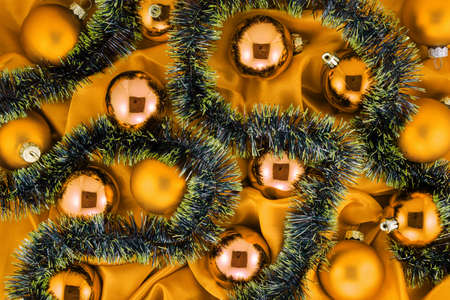 Background of golden Christmas tree balls with gold and green decorations on gold shiny silk fabricの写真素材
