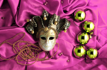 Background of golden Christmas tree balls with gold decorations and golden mask on pink shiny silk fabric with dramatic light and shadowの写真素材