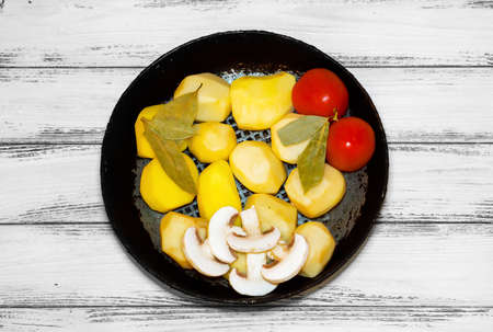 Frying pan with products for roasting: potatoes, mushrooms, tomatoes, spicesの写真素材
