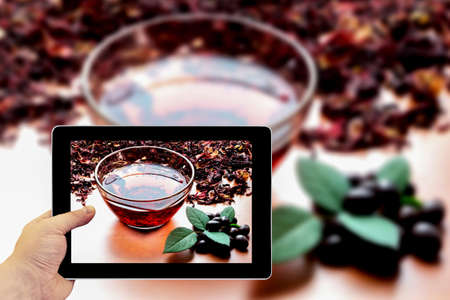 Tablet photography concept. Taking pictures on a tablet. Still life cup of black tea with mint leaves on dried karkade tea backgroundの写真素材