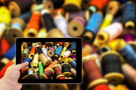 Tablet photography concept. Taking pictures on a tablet. Colored high contrasted threads for sewingの写真素材