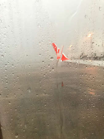 The raindrops are on the window of airplane which is in front of another plane. The blurred picture of runway that is raining outsideの写真素材