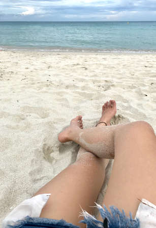 The girl who has sandy legs is laying down on the beach. Sandy beach tourist who wearing Anklet...