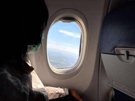 A girl in a medical mask looks out of an airplane window.