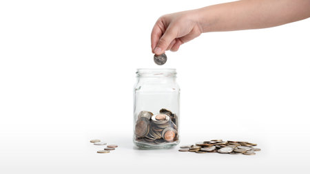 The child's hand is putting a coin into a glass jar isolated on white background. money saving...