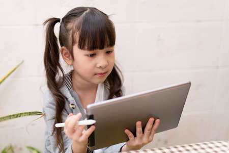 Asian girl with digital tablet and pen studying online at home. Education and distance learning for kids. Homeschooling during quarantine. Stay at home entertainment.の写真素材