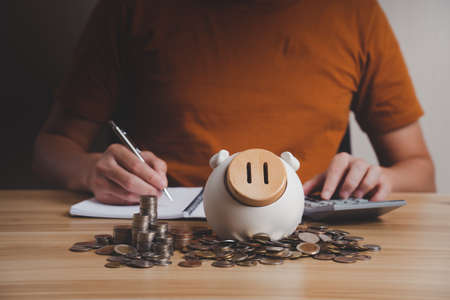 Businessman with pile of money and piggy bank and savings calculator on his desk. financial and business planning, fund, pension, business incomeの写真素材