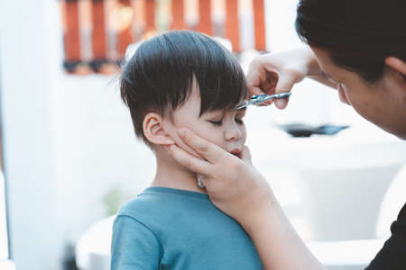 Asian mother cuts her son's hair by herself at home. Happy haircut ideas for kids. Mothers are happy to cut their children's hair.の写真素材