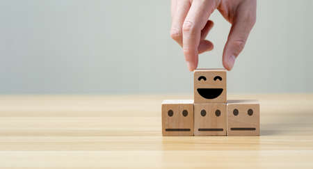 customer services best. Businessman's hand selects a smiley face on a wooden block. 5 star satisfaction, Excellent business rating experienceの写真素材