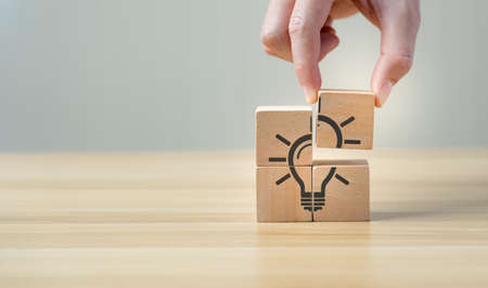 Idea and creativity concept. Hand of business selected wooden cube block with light bulb icon symbol...