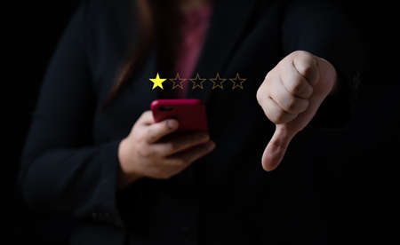 Business women select bad face emoticon on virtual touch screen at smartphone. Bad review, bad service dislike bad quality, low rating, social media not goodの写真素材