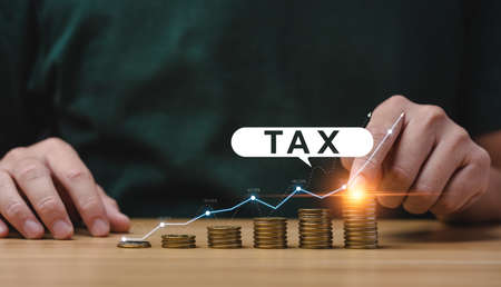 Tax deduction planning concept. Expenses, account, VAT, income tax, and property tax, pay tax. Businessman's hand and pile of coins on the table.の写真素材