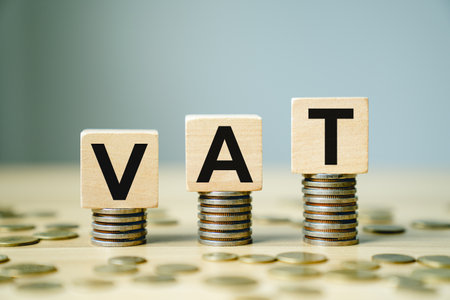 VAT Concept with Wooden Blocks Placed on Stacks of Coins Representing Value Added Tax in Finance, Taxation, and Business Economicsの写真素材