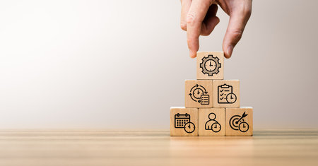 Time management and productivity concept with hand arranging wooden blocks stacked in pyramid structure, featuring icons of clock, checklist, calendar, target and workflow for planning, organizationの写真素材