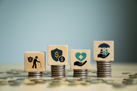 Financial and insurance planning concept with wooden blocks on stacked coins showing retirement, money protection, health care, family coverage, symbolizing wealth security, savings, risk managementの写真素材