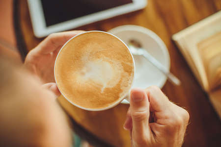 Men's hands hold  coffee and book on  tableの写真素材