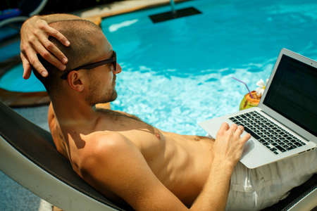 A man working at the computer next to the poolの写真素材