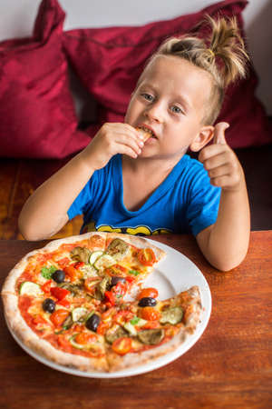 4 year old boy eating pizza in a restaurantの写真素材