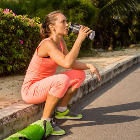 Young woman resting after exercising and holding water bottle