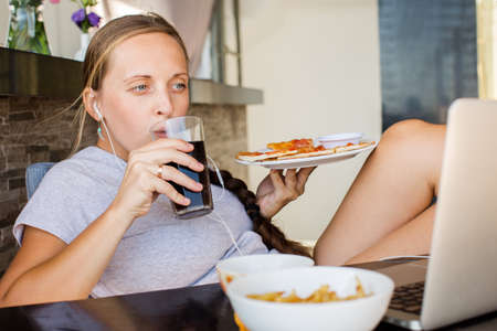 Woman works at the computer and eating fast food. Unhealthy Lifestyleの写真素材