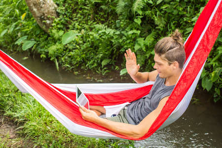 Man in hammock working on laptop during summer holidays.の写真素材