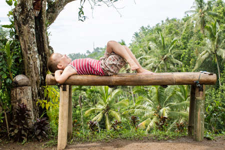 Boy lying on the bench against the backdrop of the mountains in Ubud, Baliの写真素材