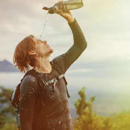 Outdoor portrait of Young man looking on Batur volcano and Agung mountain view at morning from Kintamani, Bali, Indonesia and drink waterの写真素材